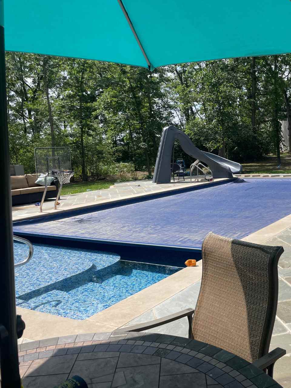 Covered pool installed by a pool installer in Waterford, Wisconsin with a slide in the background.
